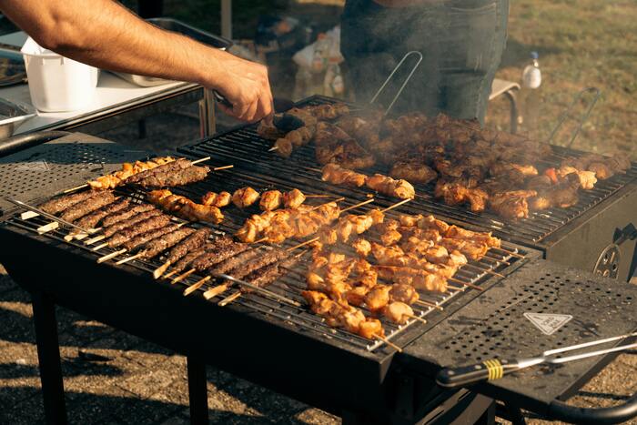 Churrasqueiro virando espetinhos variados de carne e frango em uma grelha de churrasco a carvão
